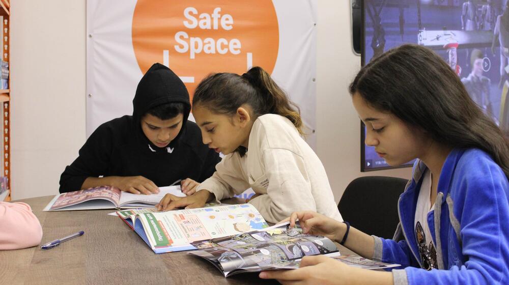 Trois jeunes, un garçon et deux filles, sont assis·e·s et lisent ensemble dans un espace sûr.