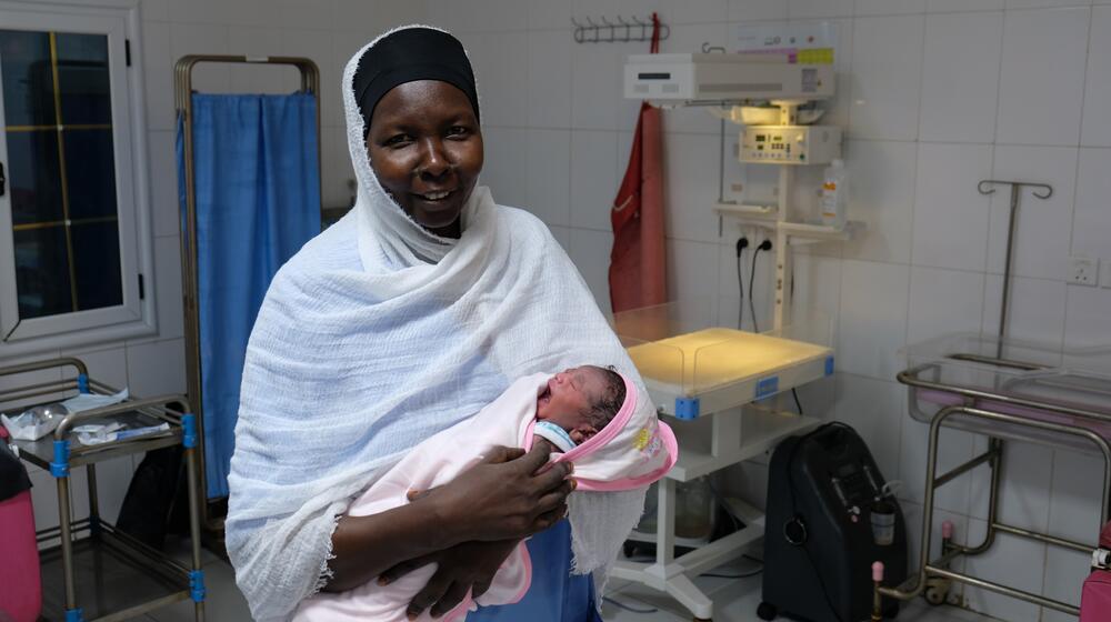 A midwife happily smiles as she holds a newborn baby in a hospital.