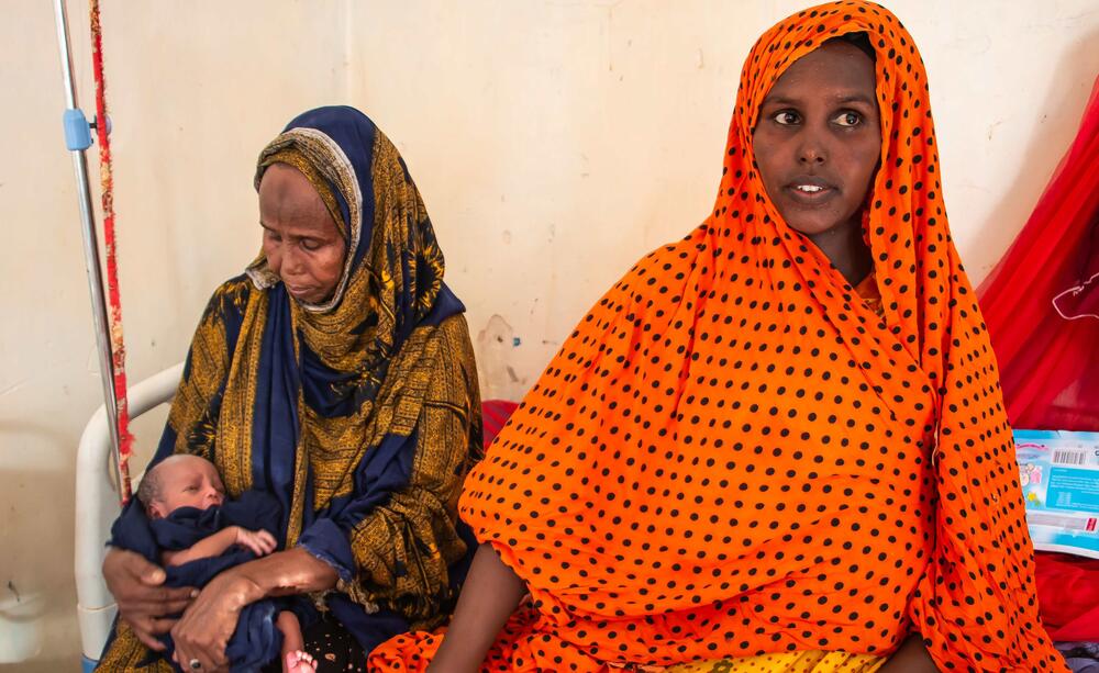 Two women sit with a newborn child.