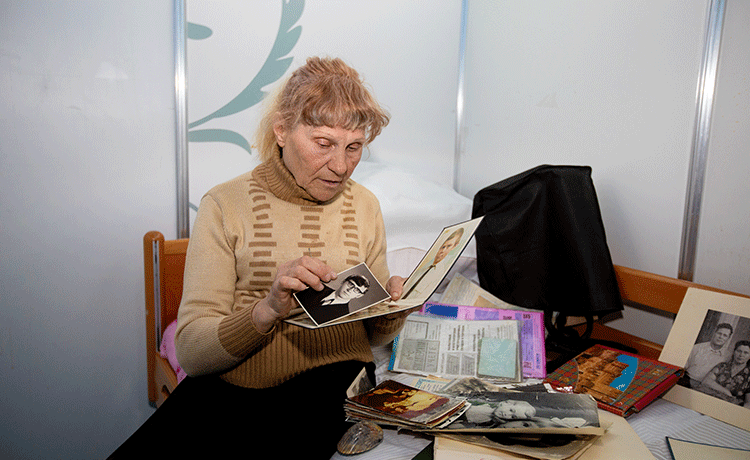 Una mujer mayor se sienta en su cama y mira las fotos.