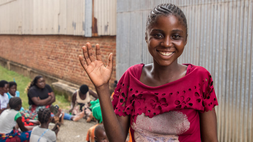 Una niña sonríe y saluda mientras asiste a una sesión de espacio seguro en un campamento temporal en Malawi.