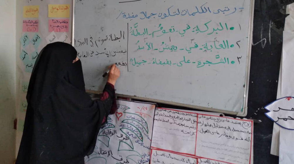Young girl in black hijab writes on a whiteboard in a classroom