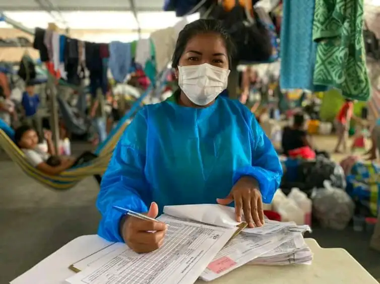 Une agente de suivi de santé vêtue d’une blouse médicale et d’un masque remplit des papiers.
