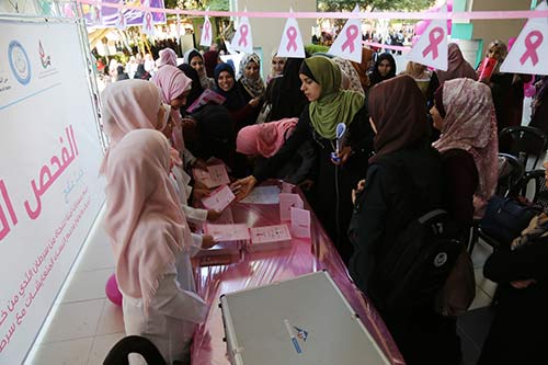 Women in pink hijabs speak to women fathering around a table with a pink tablecloth.