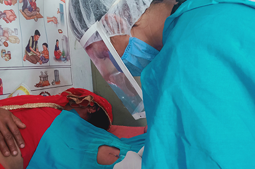 Kabita Bhandari, wearing a face mask, face shield, hair covering and protective gown, places a long-acting contraceptive implant into the arm of a client.