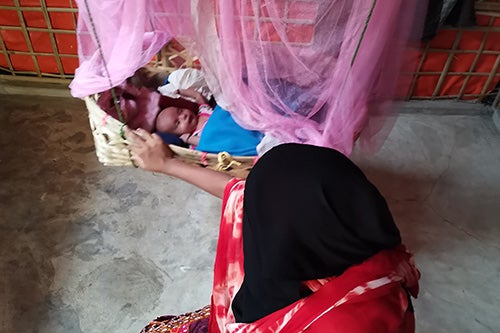 A woman wearing a black headscarf rocks a baby in a basket.