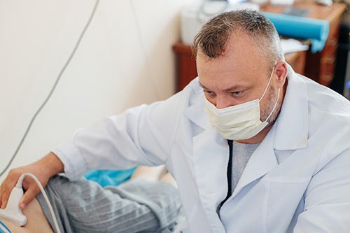 Dr. Ieriomin performs a scan on a patient's abdomen. He is wearing a face mask.