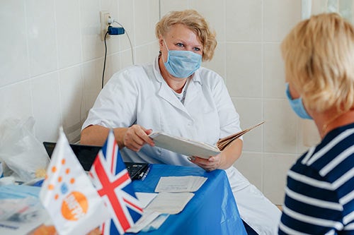 Dr. Kyslytsia holds a patient file while she speaks with a woman. Both are wearing masks.
