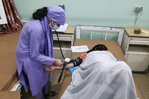 A midwife in purple scrubs takes the blood pressure of a pregnant woman.