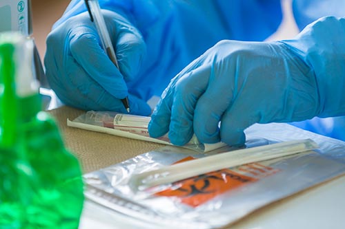 A health worker in gloves labels a vial of blood.