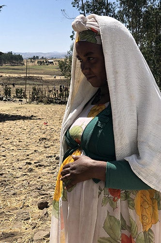 Hiwot* holds onto her pregnant midsection standing on the dry straw-strewn ground near the displacement site.