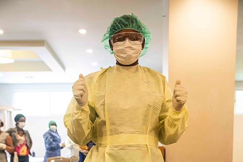 A health worker tries on a protective gown, googles, bonnet, face mask and gloves.
