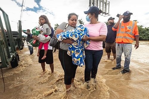 Women carry their children through ankle-deep flood water.