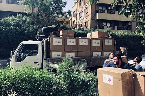 Young men load large cardboard boxes onto a flatbed truck. 