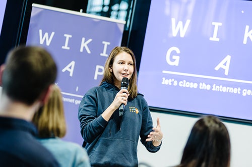 Nataliia Koshovska speaks to a group of  young people. She is holding a microphone and wearing a sweatshirt with the UNFPA logo.