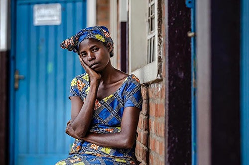 A woman in a blue patterned dress rests her head in one hand as she looks into the camera.