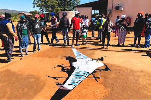 Community members stand around a large square landing pad of packed dirt. 