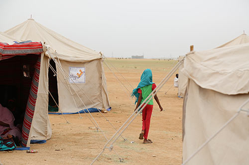 A girl walks through a tent settlement.