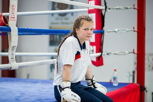 A girl in boxing gloves poses on a boxing ring.
