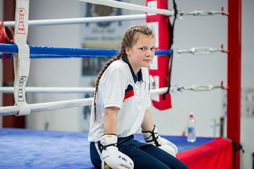 A girl in boxing gloves poses on a boxing ring. 