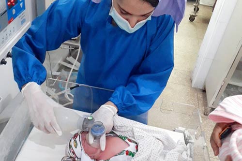 A midwifery student wearing blue scrubs attends to a newborn baby.