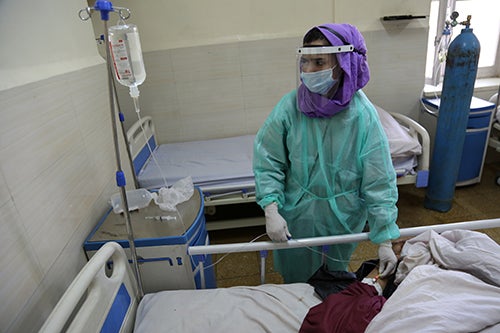 Midwife Suhaila checks on a patient. She is wearing a face mask, face shield, gloves and protective gown.