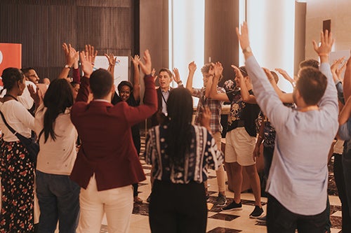 Young people stand in a circle raising their arms. They are smiling. 