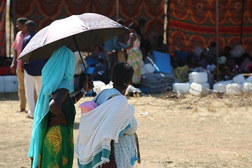 Women stand under an umbrella with an infant. 