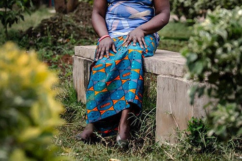 A woman sits on a bench. She is seen from waist down, without identifying details. She wears a blue blouse and skirt. 