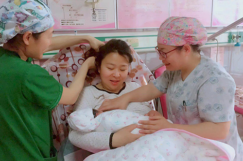 Two nurses attend to a newborn baby and postpartum mother. The mother and nurses are smiling.