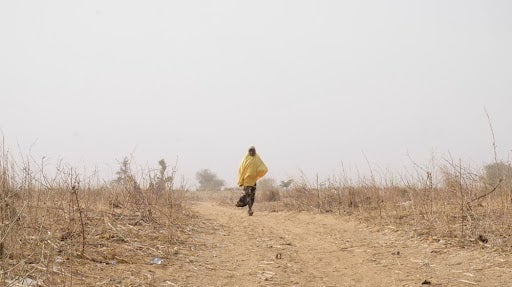 A man walks down an open dirt road. 