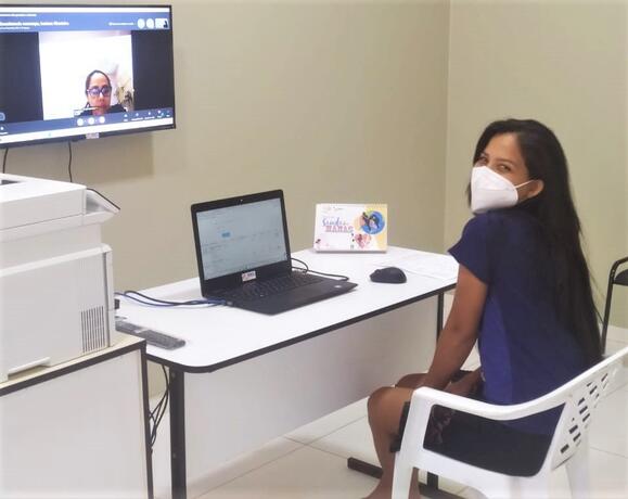 Una niña sentada en un escritorio y una silla mirando a un profesional de la salud en una pantalla de video.
