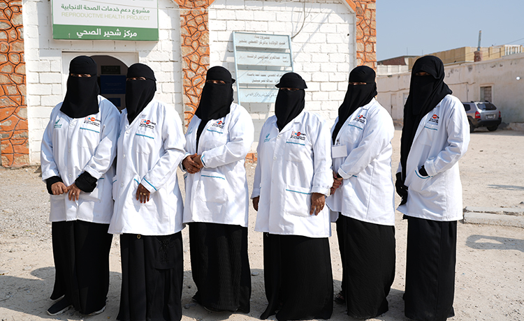Six female midwives stand in line in front of a building.