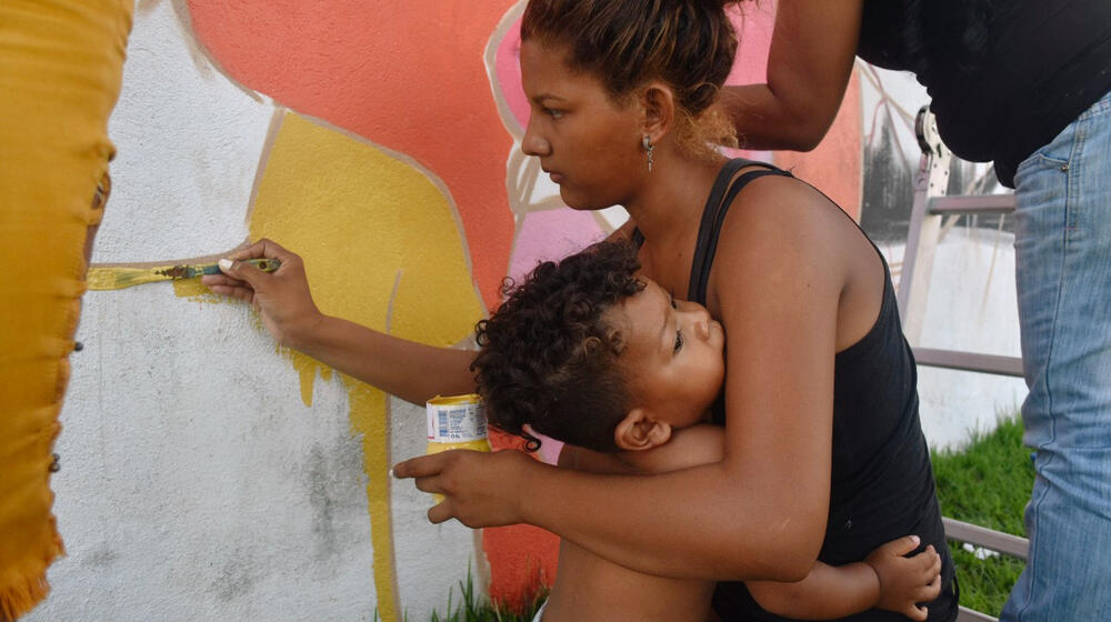 A woman paints with a baby in her arms.