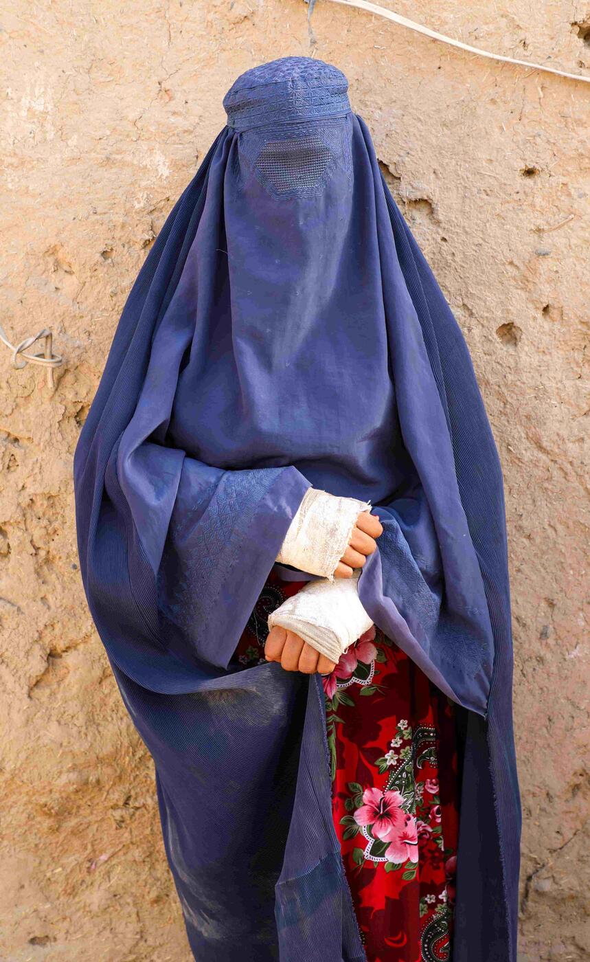A woman wearing a burqa stands in front of a wall.