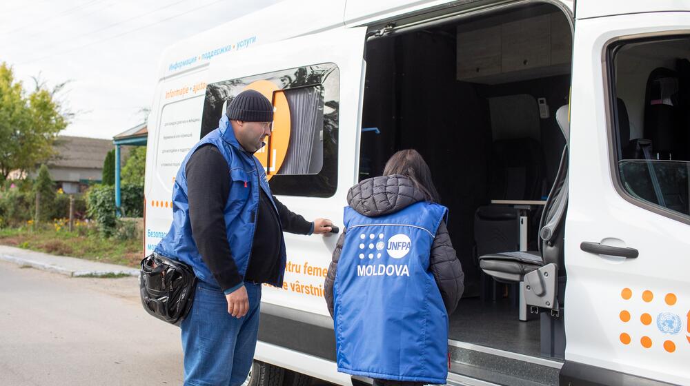 Deux agent·e·s de l’UNFPA se tiennent devant le grand véhicule d’un espace sûr mobile, qui comprend des places assises et une table.