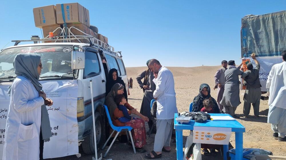 A group of people sit beside a vehicle. Medical workers assist them.