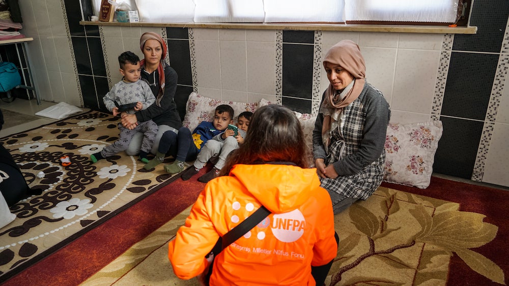 Two women sit with young children in a room and speak with a UNFPA staff member after the earthquakes that devastated Syria.