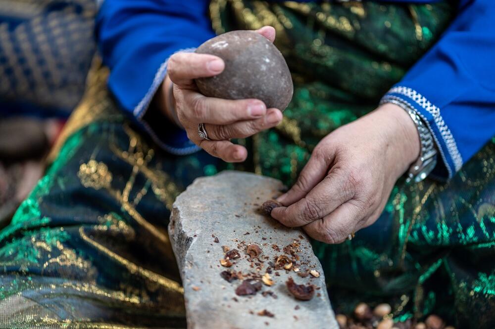 Un grupo de mujeres sentadas en el suelo producen aceite de argán golpeando con piedras las nueces del árbol sobre yunques de piedra.