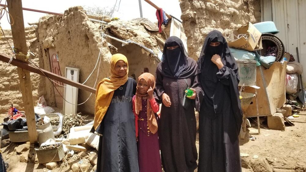 Une famille composée de femmes et de filles se tient devant un abri en ruines.