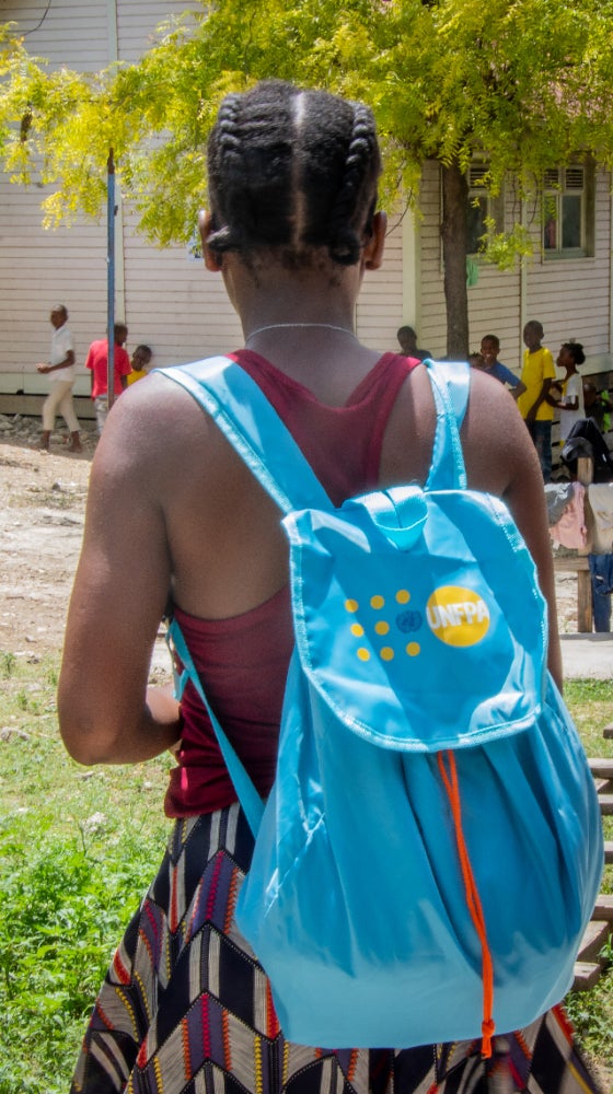 A young girl carries a backpack with supplies.