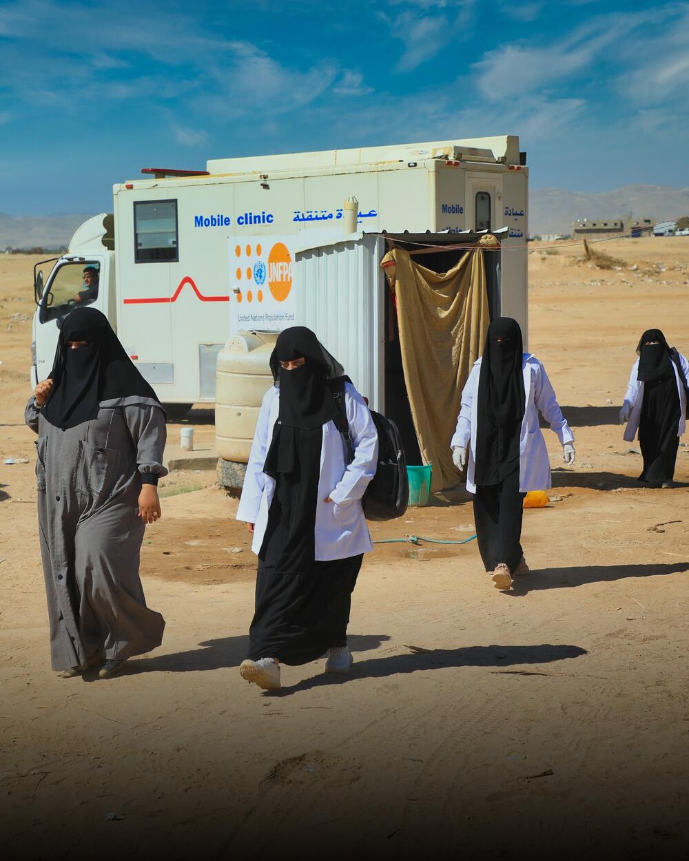 A UNFPA mobile team of women walk towards a camp for displaced people.