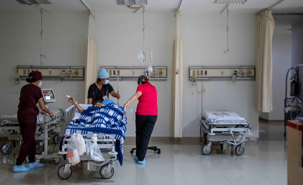 Tres trabajadores de la salud trasladan a un paciente a una cama.