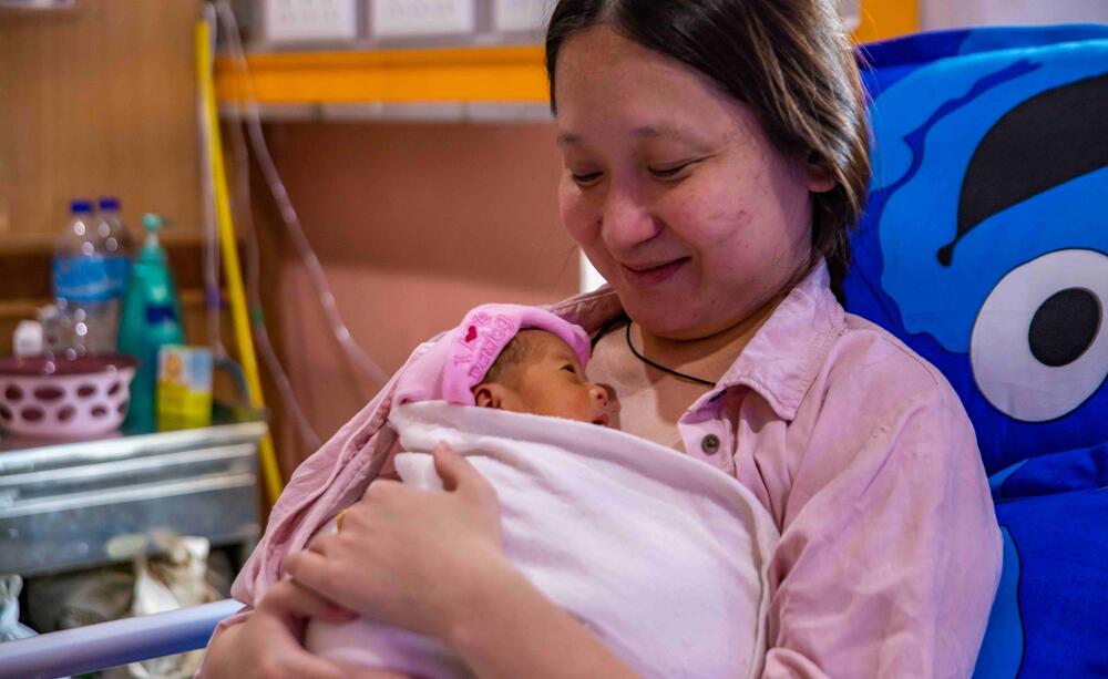 A mother smiles whilst holding her newborn baby.