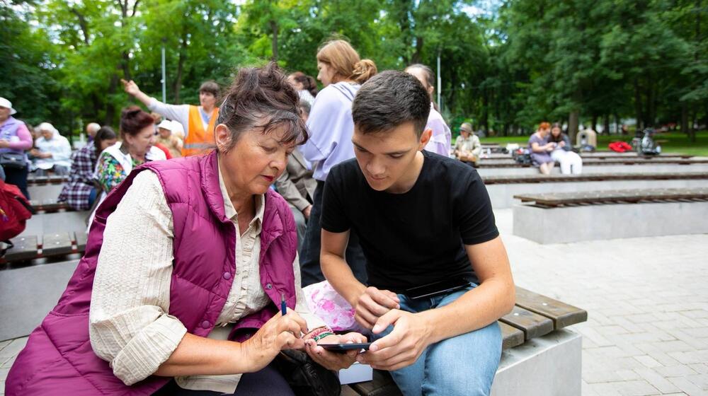 A young man assists a woman with her mobile phone.