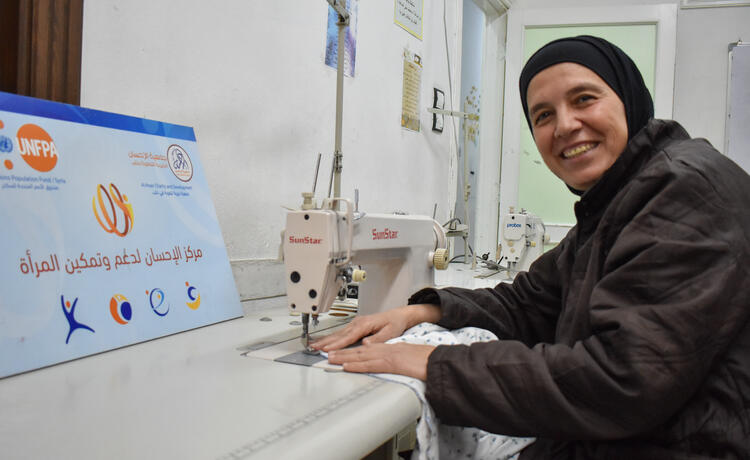 A woman smiles and uses a sewing machine in a safe space building.