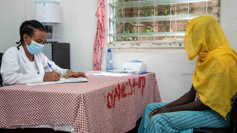 An anonymous woman sits at a 'One stop' desk with a doctor who is writing notes.