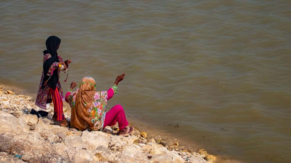 Two women sit by floodwater.