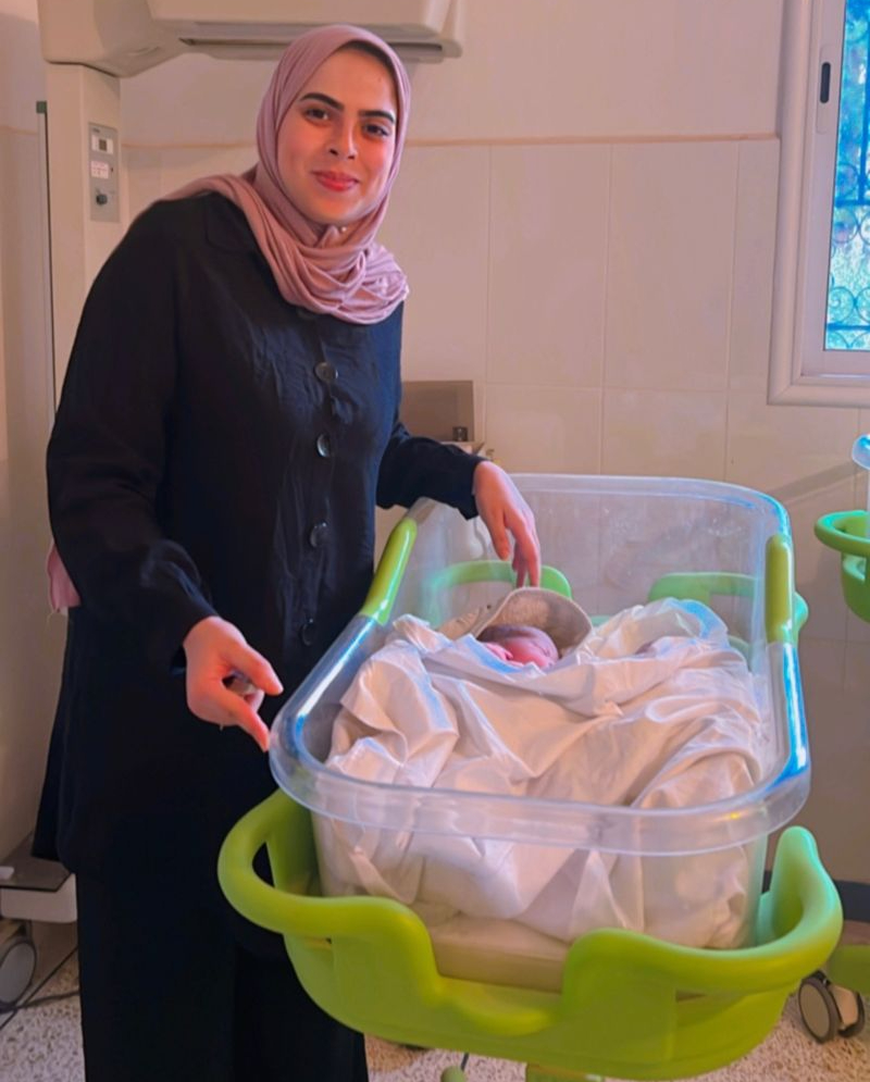 Une sage-femme sourit, debout à côté d’un nouveau-né dans un hôpital.