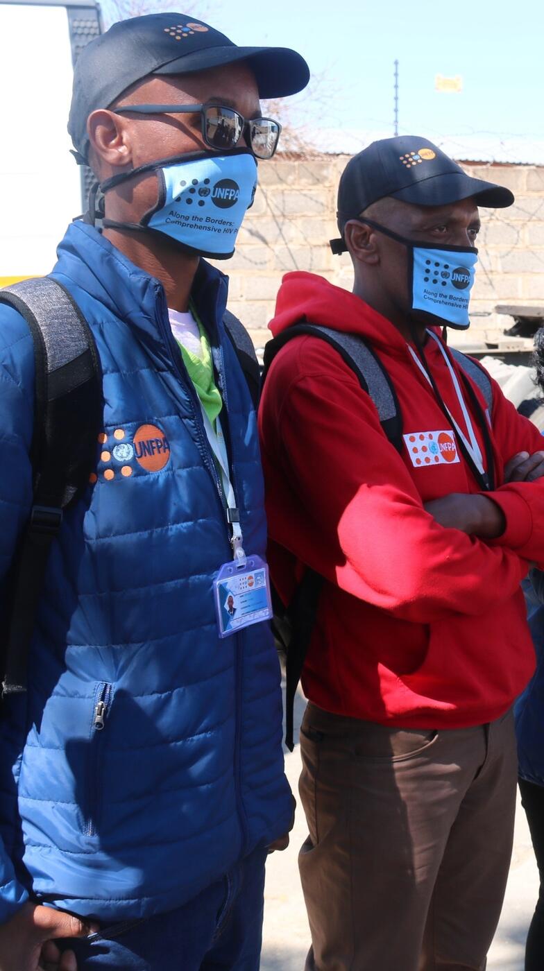 Two men stand wearing UNFPA clothing.